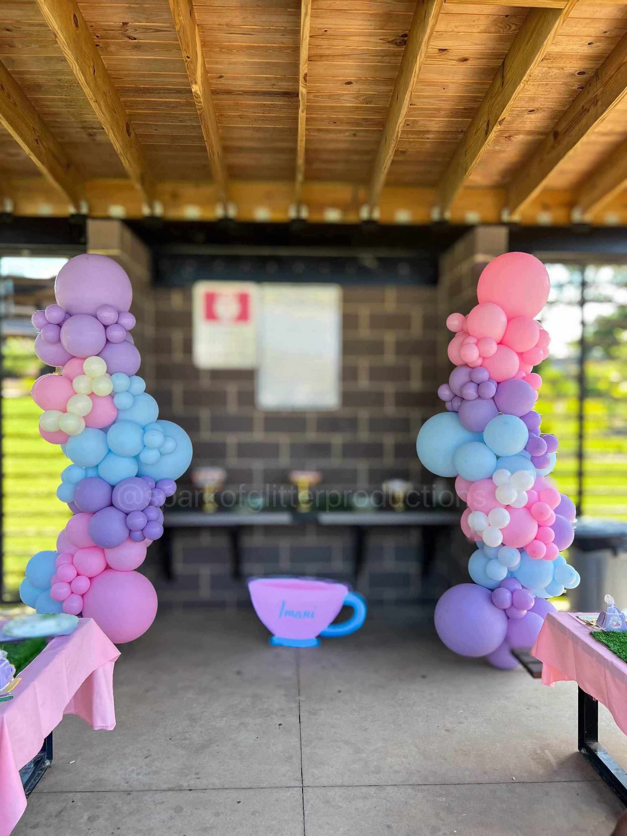 Balloon arches in pastel colors with a small blue teacup decoration on a wooden deck.