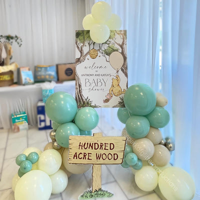 Balloon arch with a sign reading 'Hundred Acre Wood' at a baby shower.