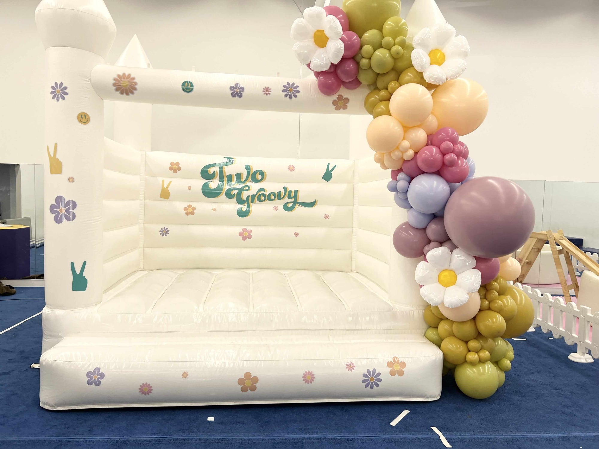 Inflatable slide with 'Two Groovy' branding and floral balloon arch.