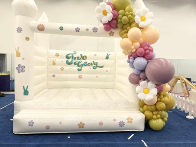 Inflatable slide with 'Two Groovy' branding and floral balloon arch.