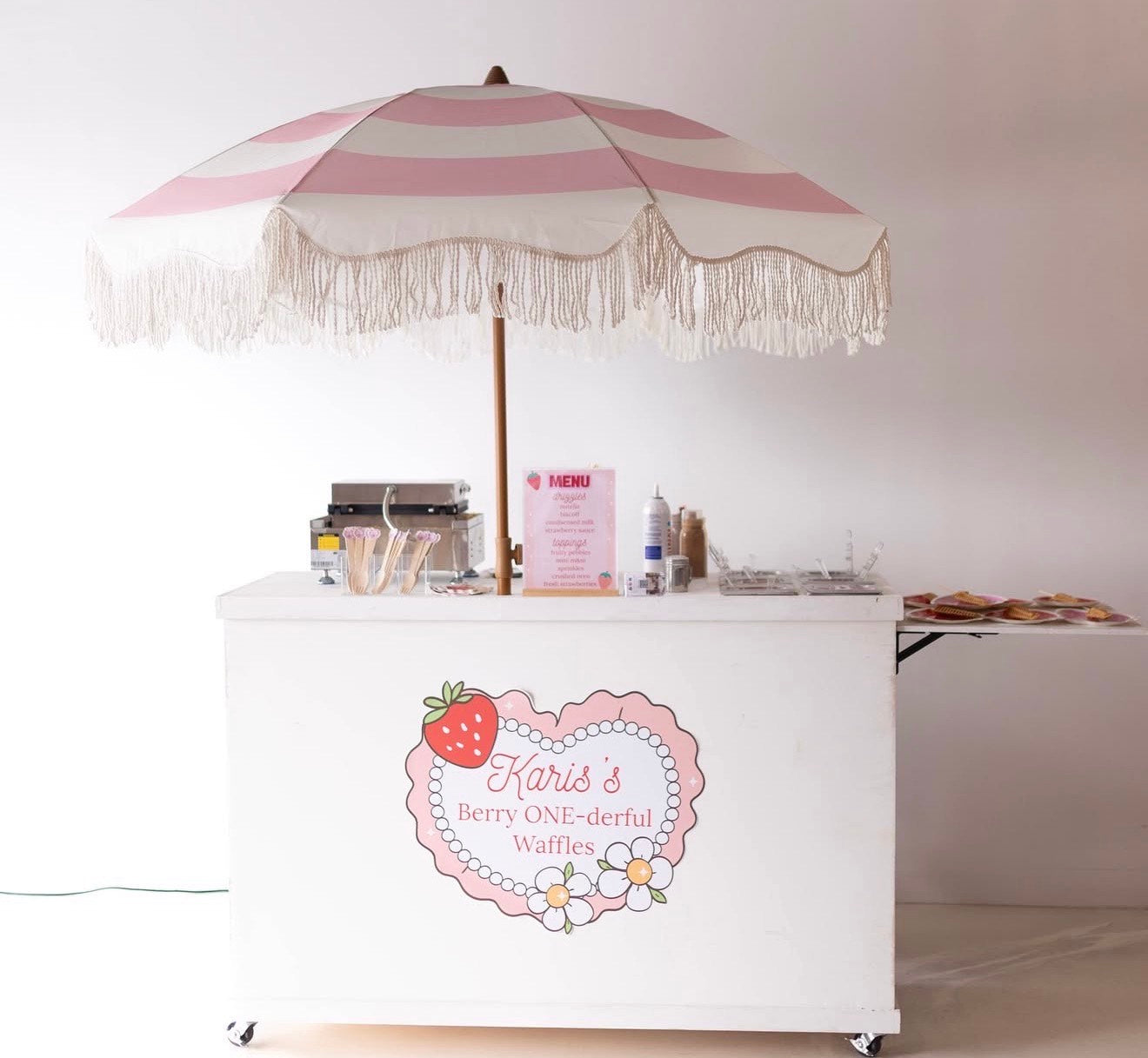 Waffle cart in Atlanta with a pink and white striped umbrella labeled 'Kari's Berry ONE-derful Waffles' on a white background.