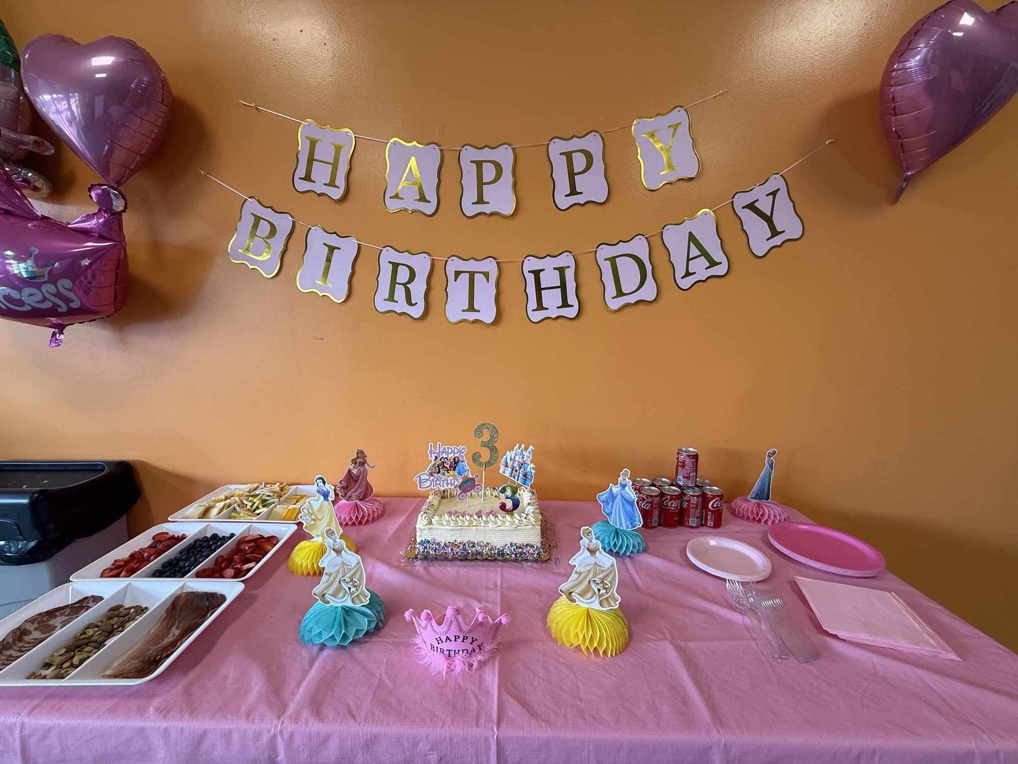 Birthday party setup with cake, decorations, and 'Happy Birthday' banner on a pink tablecloth for a 3 year old birthday party in Alpharetta GA.