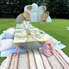 Outdoor setting with a decorated table, chairs, and a backdrop on a grassy area.