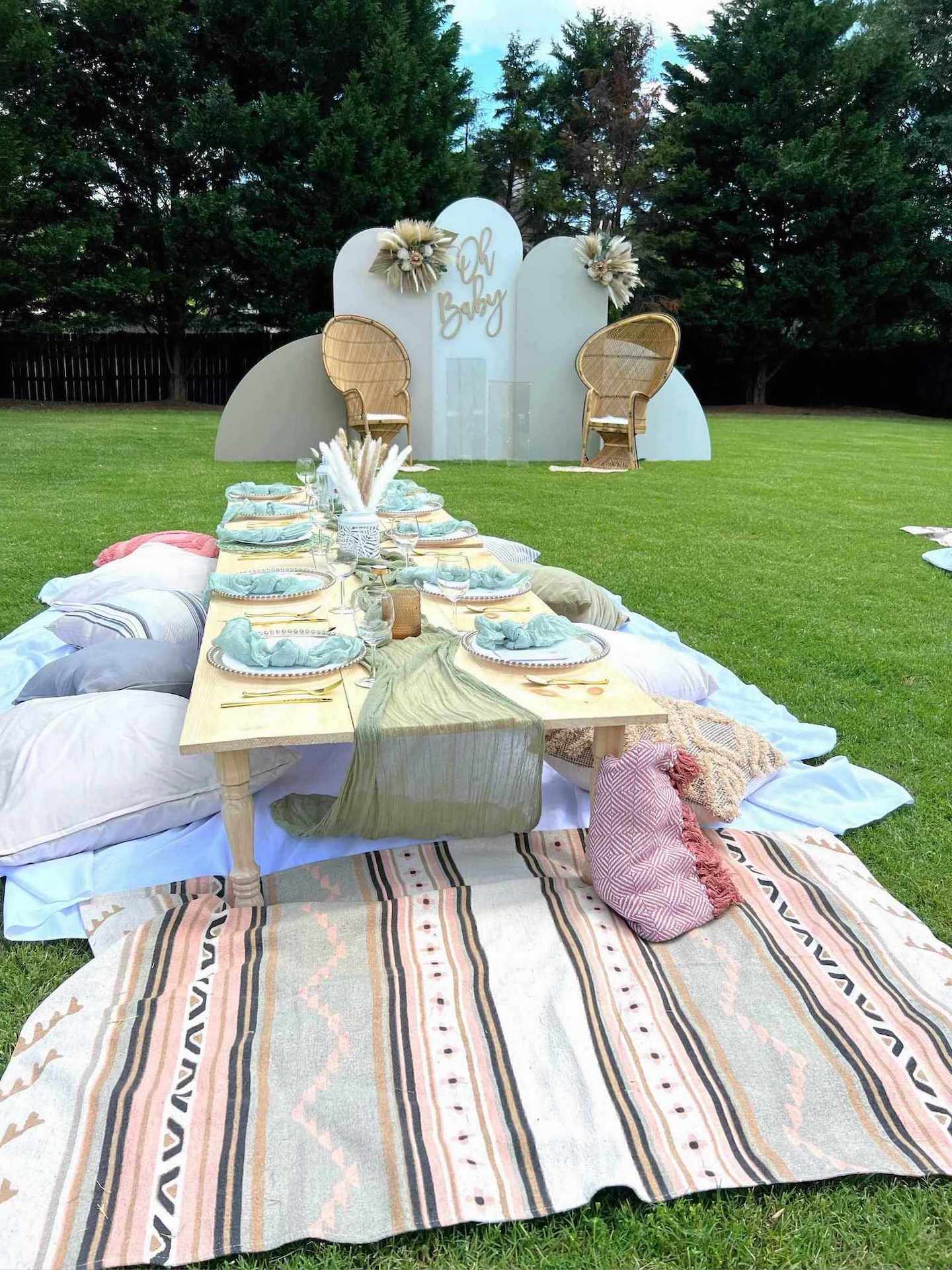 Outdoor setting with a decorated table, chairs, and a backdrop on a grassy area.