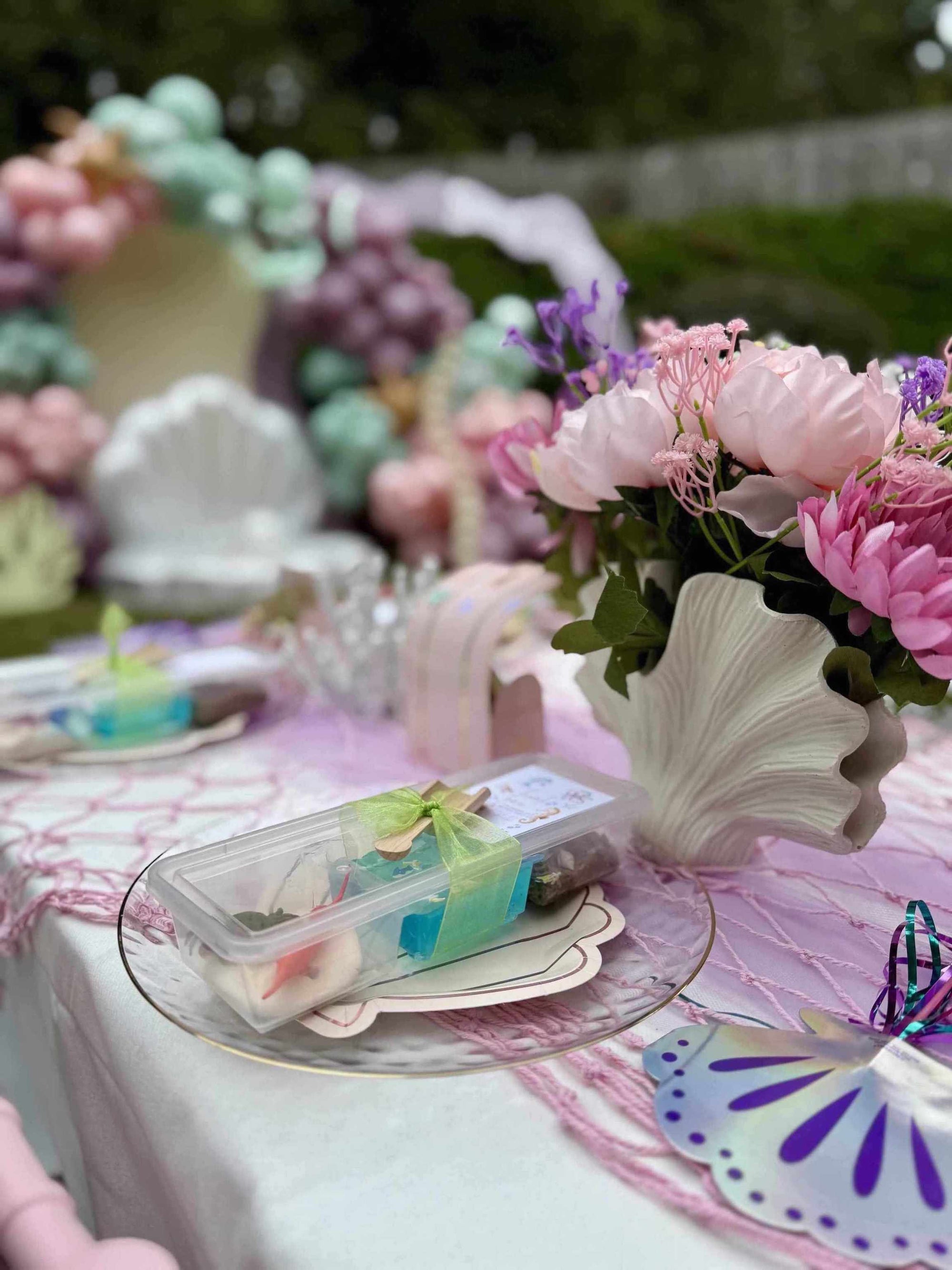 Decorative table setting with flowers and a shell-shaped vase on a pink tablecloth.