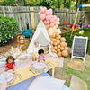 Outdoor birthday party setup with balloons, tableware, and dolls in a backyard.