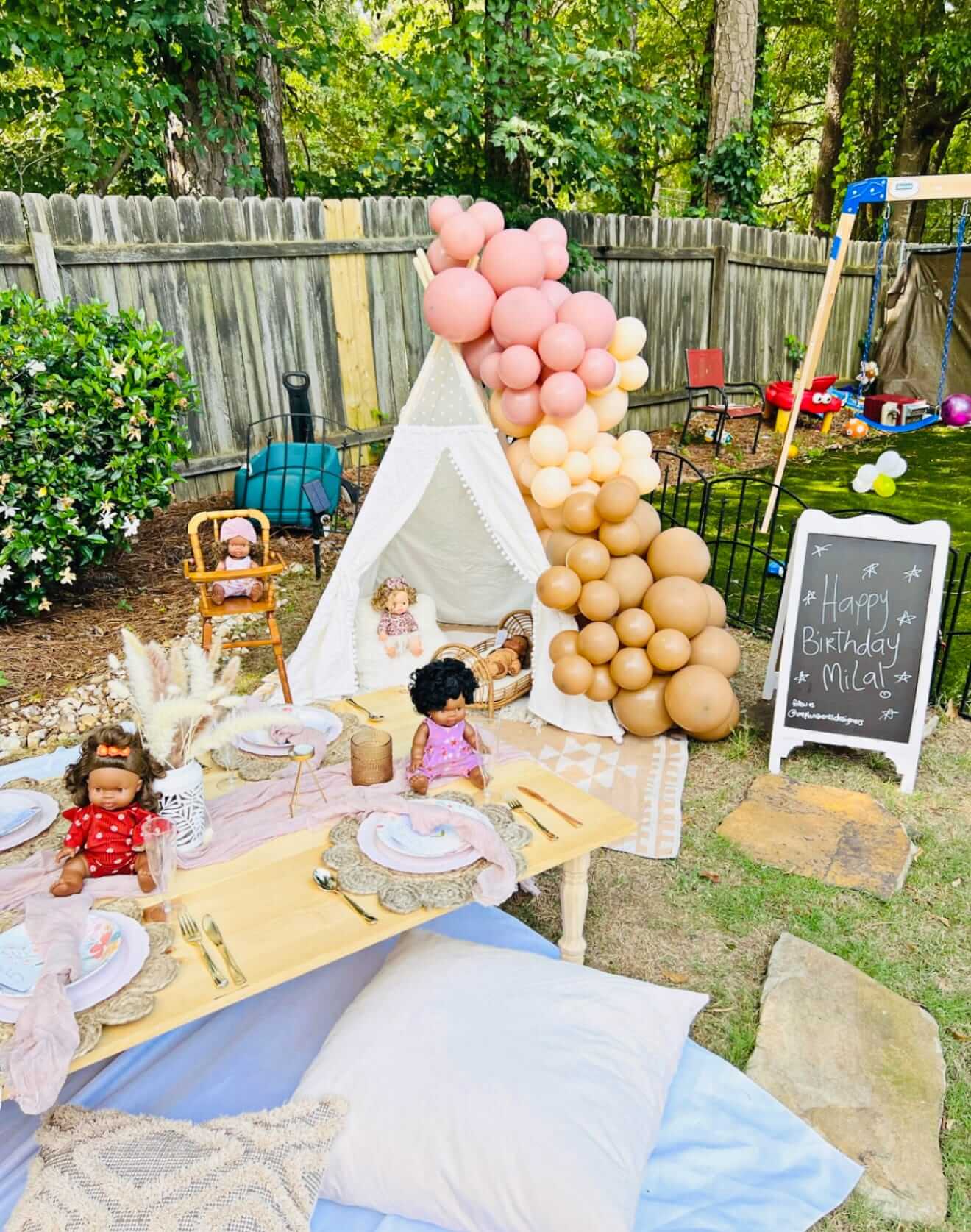 Outdoor birthday party setup with balloons, tableware, and dolls in a backyard.