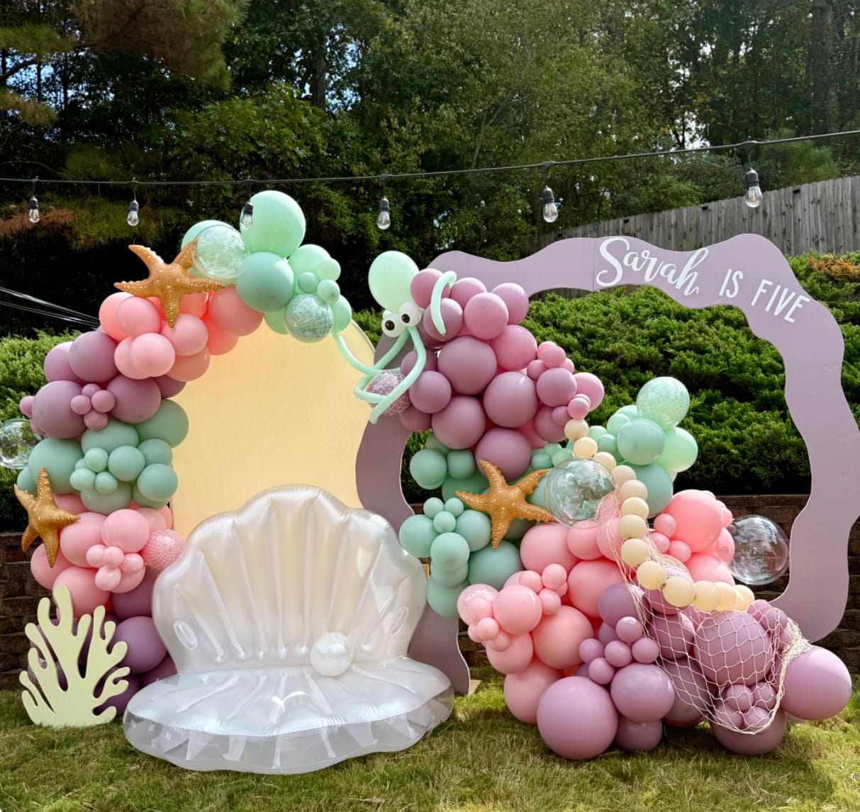 Balloon arch with ocean-themed decorations including a shell and starfish, set outdoors.