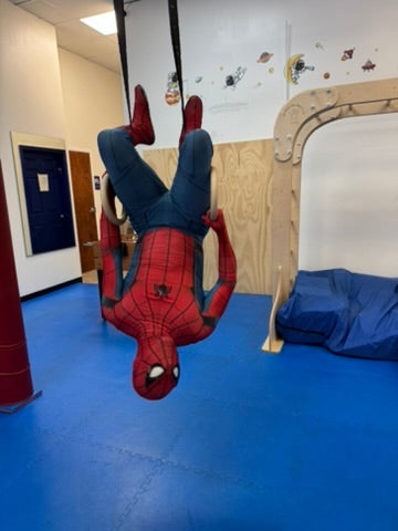 Person in Spider-Man costume hanging upside down in a room with blue floor and beige walls at and indoor birthday party for kids in Atlanta | Confetti Jar