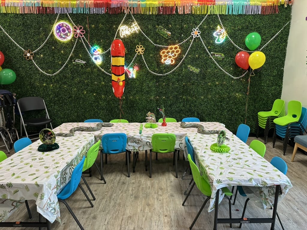 Children's party setup with tables, chairs, balloons, and decorations against a green wall at an indoor birthday party for kids in Atlanta | Confetti Jar