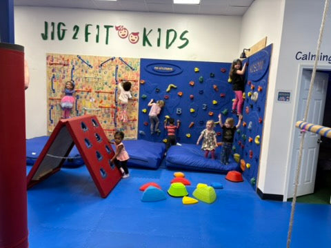 Children playing in a gymnasium with climbing wall and play equipment, featuring 'Jig 2 Fit Kids'at an indoor birthday party for kids in Atlanta | Confetti Jar
