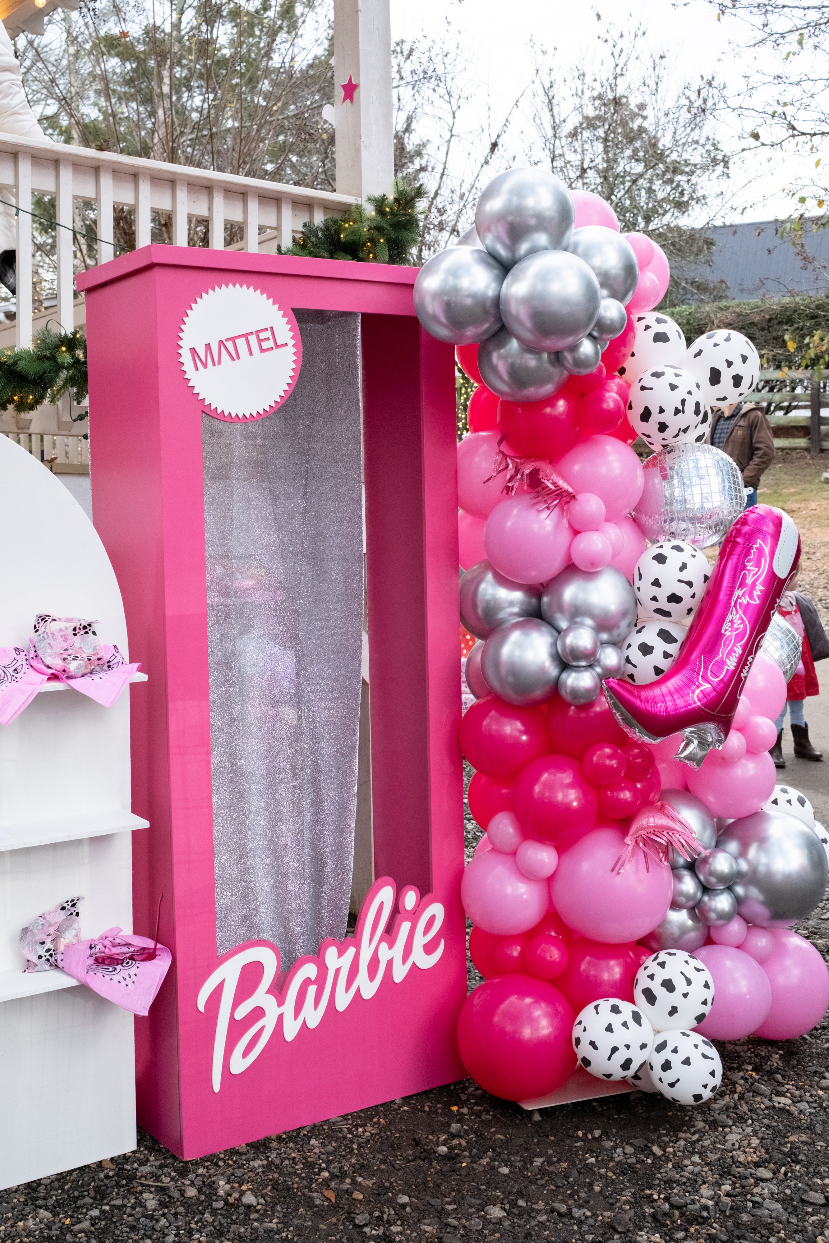 A Barbie-themed party decoration set featuring a large pink barbie photo booth frame with a clear window, a matching pink Barbie sign, and a tall balloon arrangement in pink, silver, and white with a pink high-heel balloon in Atlanta.