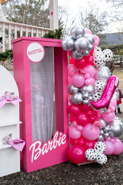 A Barbie-themed party decoration set featuring a large pink barbie photo booth frame with a clear window, a matching pink Barbie sign, and a tall balloon arrangement in pink, silver, and white with a pink high-heel balloon in Atlanta.